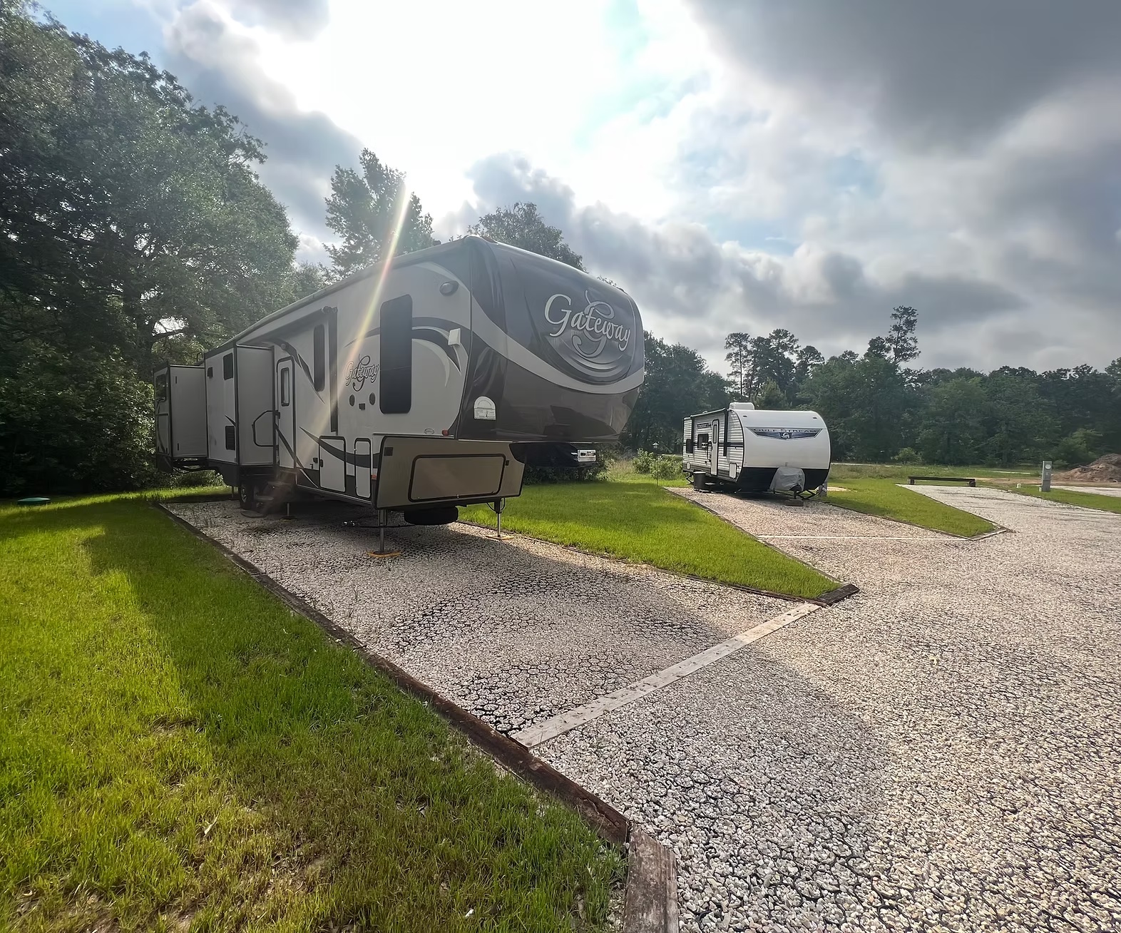 Spacious wooded RV park site with a Gateway fifth wheel and travel trailer on gravel pads